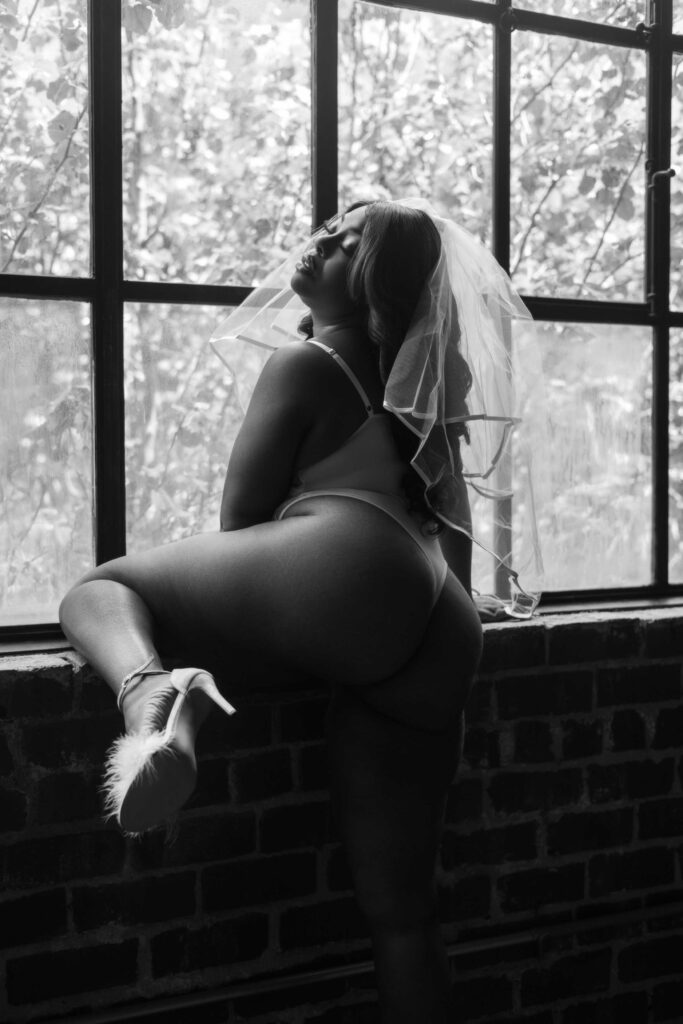 stunning woman shows off her curves to her boudoir photographer during her bridal themed photoshoot