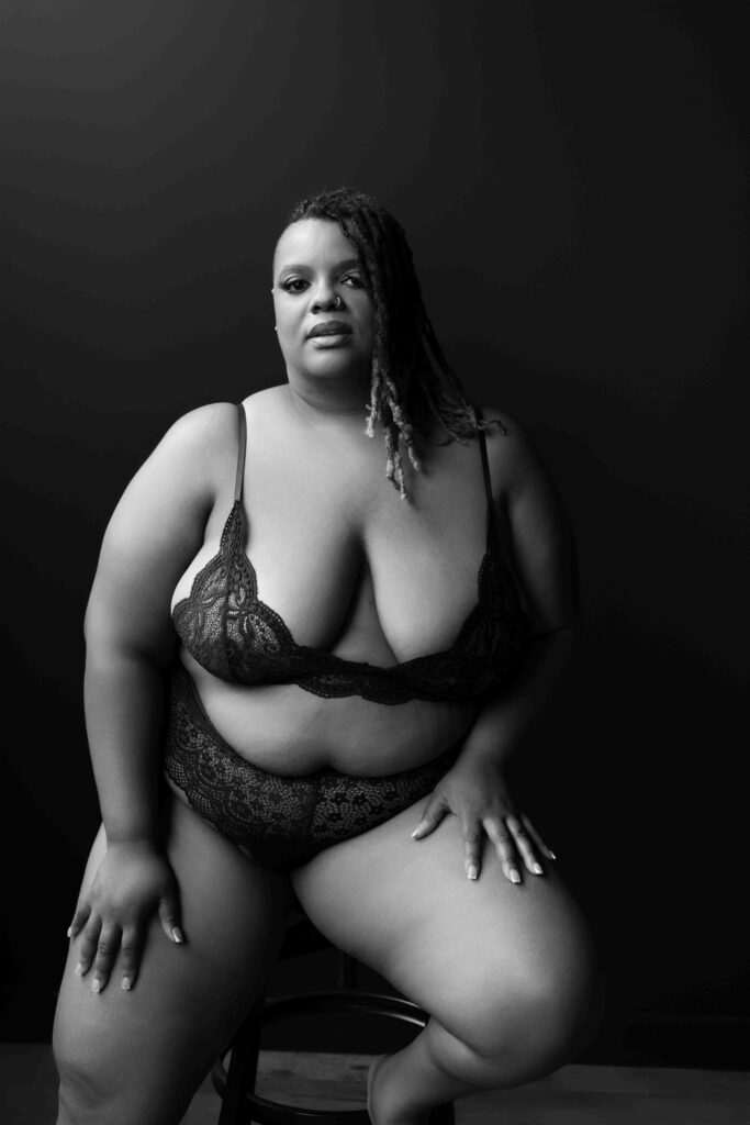 curvy woman in a 2 piece lingerie outfit sitting on a stool with one foot on the stool step, the other on the floor, looking directly in the camera