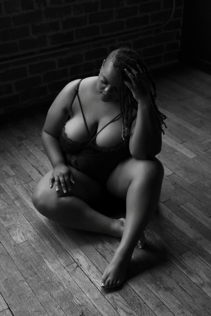 plus-size woman sitting on floor with her legs crossed in black lingerie during a boudoir shoot