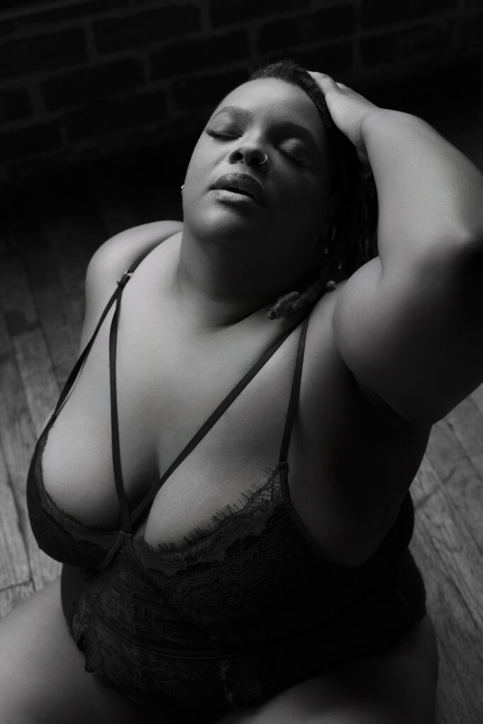 close up picture of plus-size woman sitting on the floor, head tilted back, and her hand in her hair during a boudoir shoot