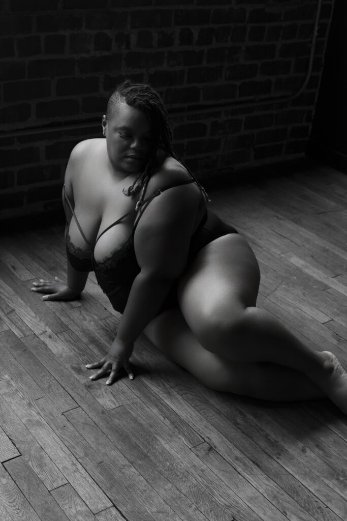 plus-size woman sitting on floor with her legs crossed in black lingerie, looking down during a boudoir shoot