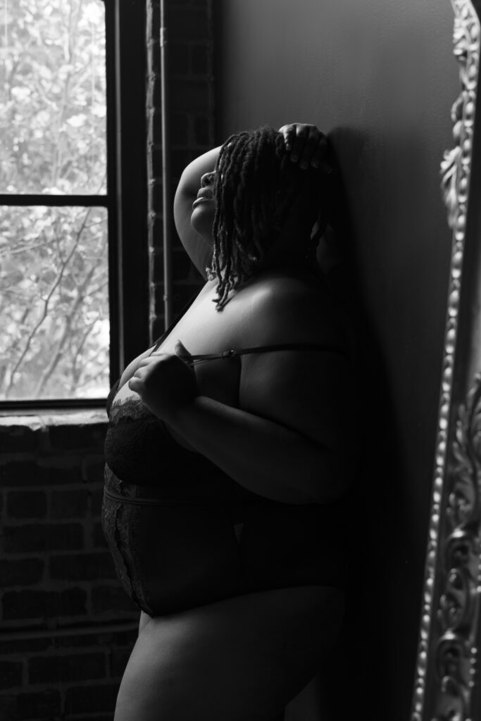 plus-size woman leaning against a wall in black lingerie during a boudoir shoot