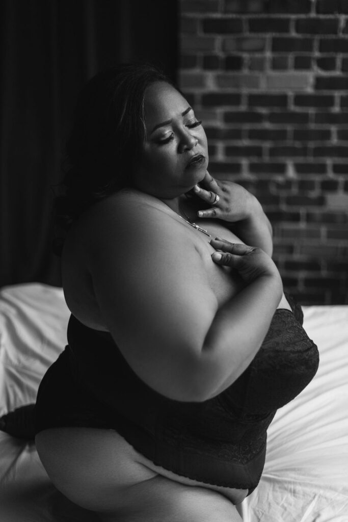 plus-size woman kneeling on a bed looking down during a boudoir shoot