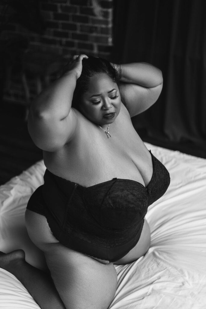 plus-size woman kneeling on a bed with hands in her hair during a boudoir shoot